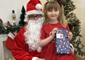 Dziecko siedzi na kolanie Mikołaja i odbiera prezent.