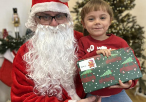 Dziecko siedzi na kolanie Mikołaja i odbiera prezent.