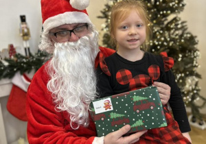 Dziecko siedzi na kolanie Mikołaja i odbiera prezent.