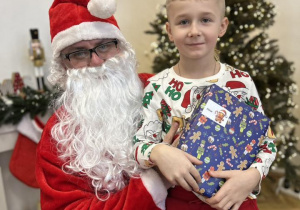 Dziecko siedzi na kolanie Mikołaja i odbiera prezent.