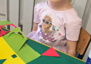 Dziewczynka siedzi przy stoliku, przed nią na stoliku są pocięte figury geometryczne.