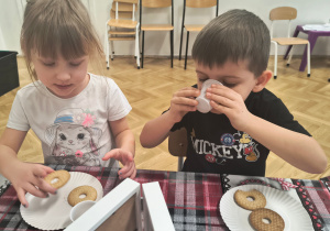 Dziewczynka je ciasteczka, chłopczyk pije herbatkę.