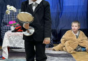 Chłopiec przebrany w garnitur i w białych okularach patrzy w lusterko.