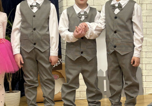 Trzech chłopców ubranych w garnitury stoją na tle dekoracji.