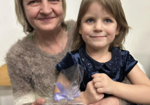 Dziewczynka siedzi u babci na kolanach, uśmiechają się.