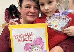 Dziewczynka siedzi u babci na kolanach, uśmiechają się.