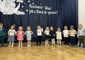 Dzieci stoją w półkolu na tle dekoracji.