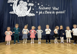 Dzieci stoją w półkolu na tle dekoracji.