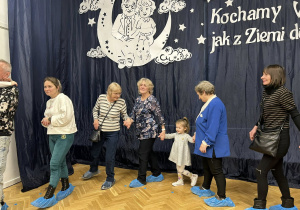 Dzieci razem z dziadkami i rodzicami trzymają się za ręce i tańczą w dużym kole.