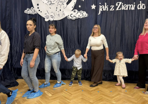 Dzieci razem z dziadkami i rodzicami trzymają się za ręce i tańczą w dużym kole.