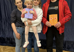 Babcia trzyma na rękach wnuczkę i razem z mamą i dziadkiem się uśmiechają.