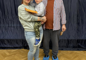 Mama trzyma syna na rękach i razem z dziadkiem się uśmiechają.