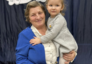 Babcia trzyma wnuczkę na rękach.