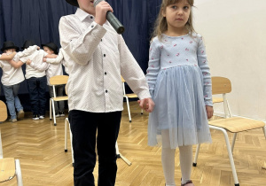 Dziewczynka i chłopiec stoją na środku. Chłopiec mówi wierszyk.