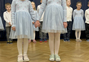 Dwie dziewczynki stoją na tle dekoracji i śpiewają piosenkę.