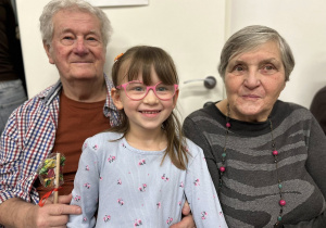 Dziewczynka siedzi pomiędzy Dziadkami, uśmiechają się.