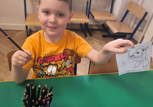 Chłopiec trzyma kolorowankę i kredkę.