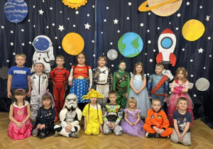 Zdjęcie grupowe - grupa IV w strojach karnawałowych stoją na tle kosmicznej dekoracji.