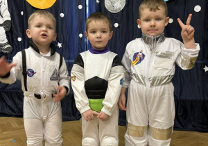 Trzech chłopców w strojach astronautów uśmiechają się.