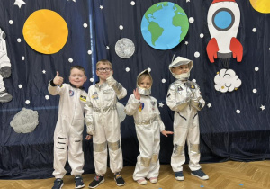 Trzech chłopców i dziewczynka w strojach astronautów uśmiechają się.