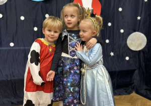 Dwie dziewczynki i chłopiec przytulają się do siebie, uśmiechając się.