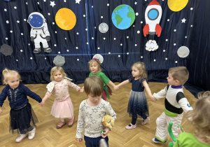 Dzieci z grupy pierwszej tańczą w kółeczku, trzymając się za ręce.