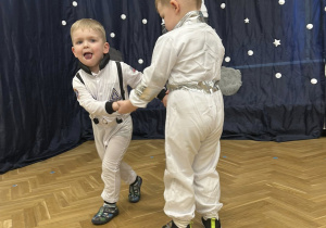 Dwóch chłopców w strojach astronautów tańczą w małym kółeczku.