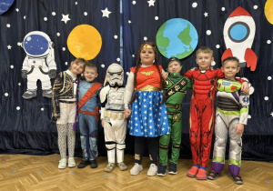 Dzieci z grupy III stoją na tle dekoracji, obejmują się i uśmiechają się.