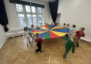 Dzieci chodzą po kole trzymając chustę animacyjną.