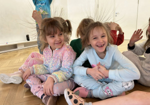 Dziewczynki siedzą pod chustą animacyjną i się uśmiechają.