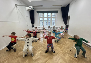 Dzieci siedzą na krzesłach z rękami wyciągniętymi.