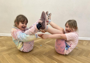 Dziewczynki trzymają się za ręce, stykają się stopami.