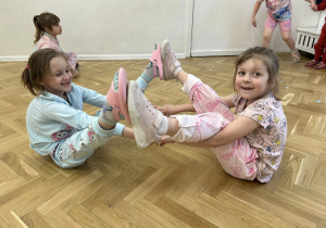 Dziewczynki trzymają się za ręce, stykają się stopami.