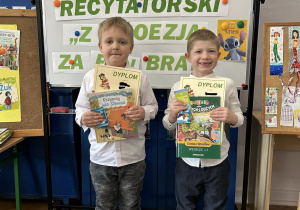 Chłopcy stoją z dyplomami na tle dekoracji.