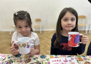 Dzieci pokazują pomalowane kubki.