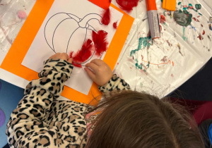 Dziewczynka wykonuje pracę plastyczną z piórek