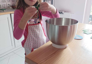 Dziewczynka w kuchni, dodaje składniki do miski.