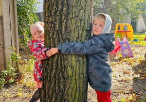Dzieci przytulają się do drzewa.