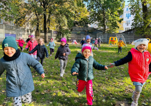 Dzieci biegają po ogrodzie przedszkolnym.