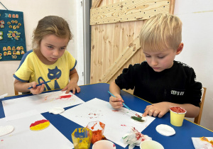 Dzieci przy stolikach malują farbami.