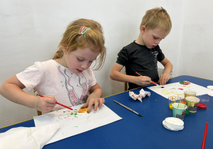 Dzieci przy stolikach malują farbami.