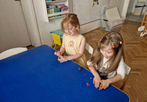 Dzieci przy stolikach wykonują pracę plastyczną.