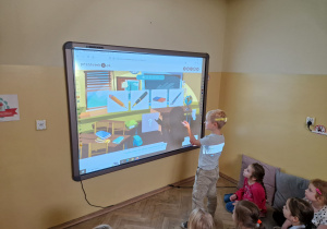 Dziecko przy tablicy multimedialnej wykonują zadanie.