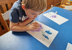 Dziecko wykonuje prace, dmuchając wodę z farbami na kartce.