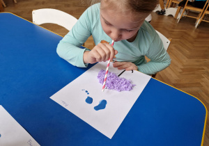 Dziecko wykonuje prace, dmuchając wodę z farbami na kartce.